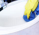 With rubber gloves and cleaning cloth cleaning a white glistening sink.